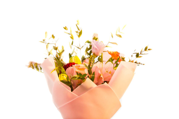 Ένα ντελικάτο μπουκέτο από διαφορετικά λουλούδια σε ένα ανοιχτό ροζ περιτύλιγμα στέκεται σε ένα ελαφρύ φόντο σε ένα σπιτικό περιβάλλον. Οριζόντια φωτογραφία. - Φωτογραφία, εικόνα
