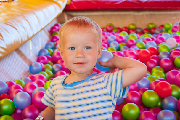 Reilu kolmen vuoden poika pelikeskuksessa pelaa uima-altaassa värillisillä muovipalloilla.
 - Valokuva, kuva