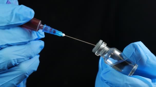 de hand van de arts houdt een spuit en een rode fles vaccin vast in het ziekenhuis op de zwarte achtergrond. Gezondheids- en medische begrippen. - Video