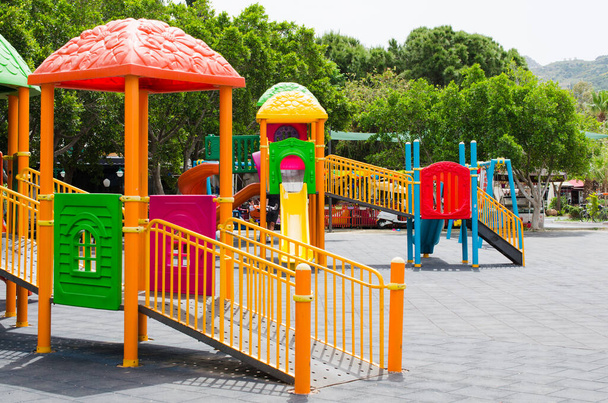 Барвисті дитячі ігрові майданчики в громадському парку в оточенні зелених дерев. Дитячий майданчик без дітей
 - Фото, зображення