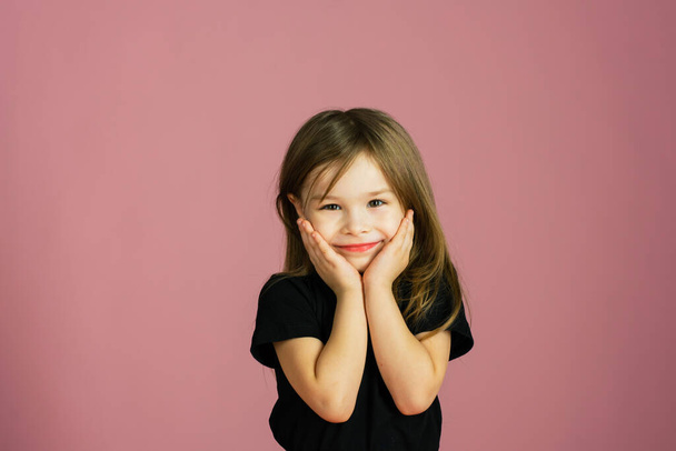 Χαριτωμένο κορίτσι με μαύρο μπλουζάκι και κόκκινη φούστα σε ροζ παστέλ φόντο κοιτάζει την κάμερα και χαμογελάει. - Φωτογραφία, εικόνα
