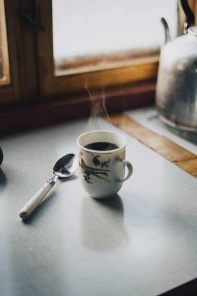 A vertical shot of a cup of coffee and a spoon on the table next to the window in Norway - Fotoğraf, Görsel
