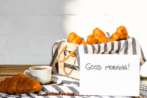 Coffee cup and buttered fresh French croissant on wooden crate. Food and breakfast concept. Morning message on white board - Foto, Imagem