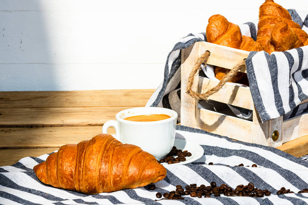 Puff pastry, coffee cup and buttered French croissant on wooden crate. Food and breakfast concept. Detail of coffee desserts and fresh pastries - Photo, Image