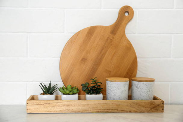 Wooden board near jars and houseplants on countertop in modern kitchen - Fotografie, Obrázek