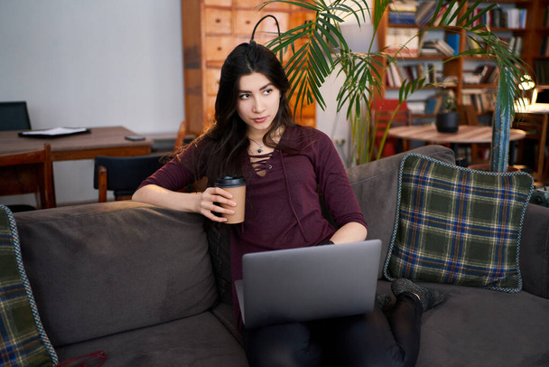 young woman working remotely from home on laptop, sitting on the couch - Photo, Image