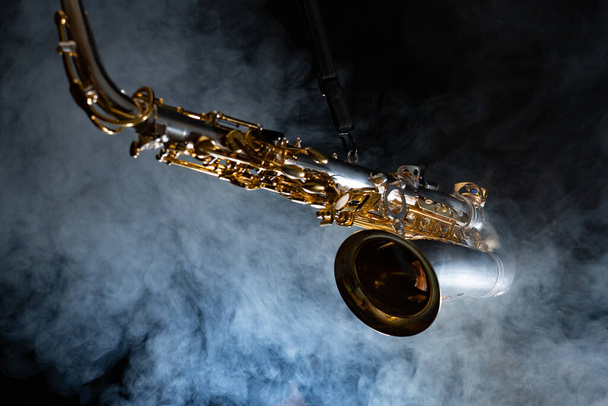 Golden shiny alto saxophone on black background with smoke. copy space - Фото, изображение