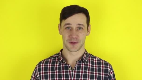 A funny, cute guy is having a video chat conversation. A portrait of a young guy, he communicates with friends via video chat. Portrait on a yellow background. - Materiał filmowy, wideo