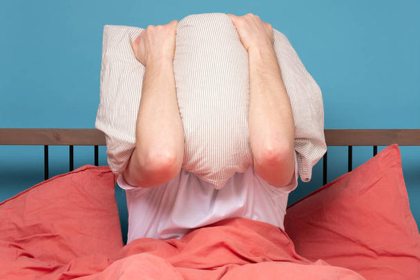 Молодий кавказький чоловік вкриває обличчя подушкою стрес. Студійний знімок
 - Фото, зображення