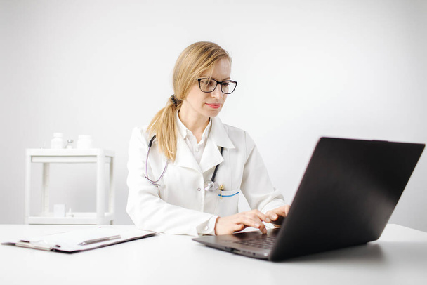 医療用制服を着た女性がオフィスでノートパソコンで作業 - 写真・画像