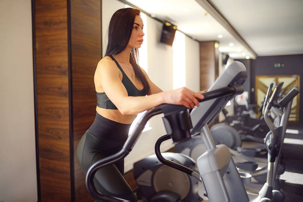 Training in the gym Fitness girl coach working on Step machine and showing her figure posing in a sports suit - 写真・画像