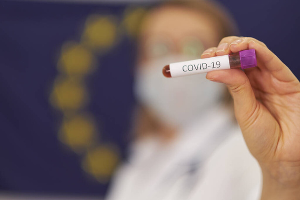 Доктор стоїть навпроти прапора Європейського Союзу. COVID-19 тест і лабораторний аналіз крові для діагностики нової інфекції корони - Фото, зображення