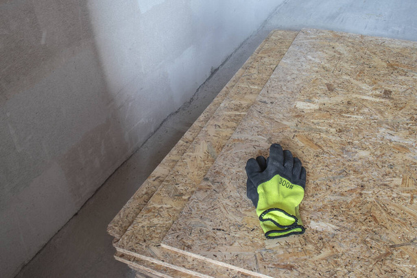 Матеріал будівельної плити OSB, виготовлений з відновленої тирси. Вони лежать в купі, на ньому лежать жовті захисні рукавички. Крупним планом
. - Фото, зображення