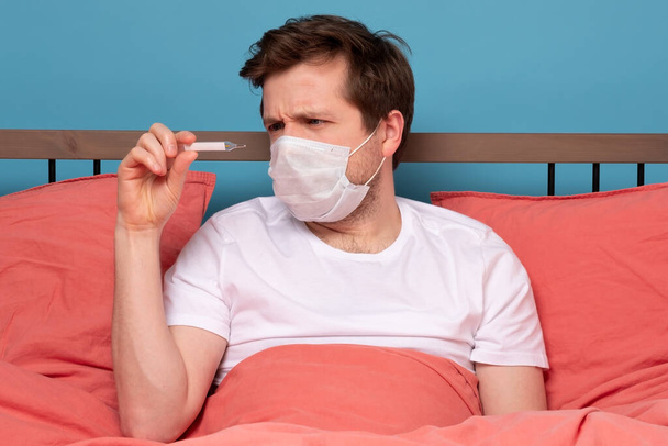 Хворий чоловік лежить на ліжку, перевіряючи температуру вдома. Студійний знімок
 - Фото, зображення