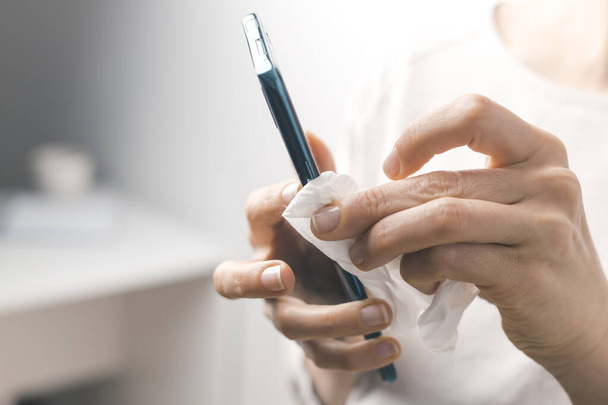 Femme désinfecte le téléphone avec de l'alcool contre les bactéries virales. Écran antiseptique pour smartphone
. - Photo, image