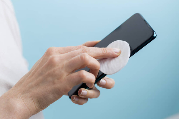 Woman disinfects the phone with alcohol against viral bacteria. Antiseptic processing smartphone screen. - Foto, Bild