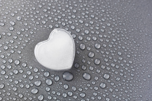 A close up image of a heart shaped ice cube melting on a grey metal background. - Fotografie, Obrázek