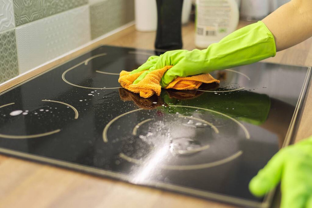 Woman hand in gloves cleaning kitchen electric ceramic hob, polishing glass with microfiber cloth - Foto, imagen