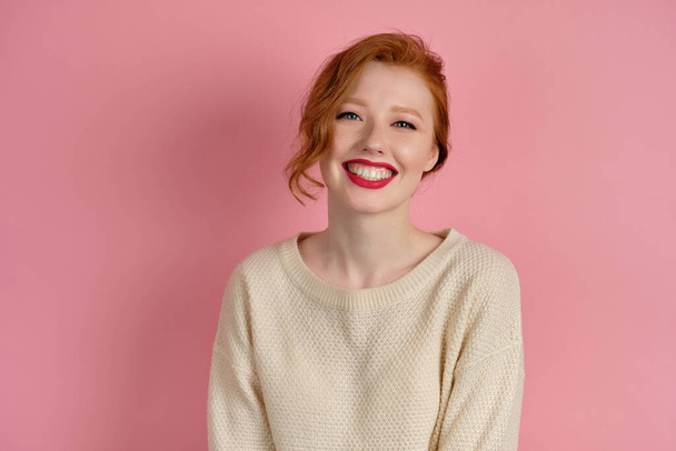 Cute red-haired girl with red lipstick and collected hair smiles beautifully on a pink background - Foto, Imagem