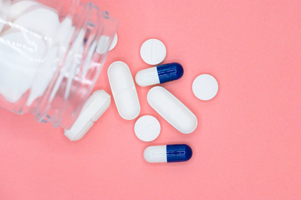 Close-up van pillen morsen uit de pil fles op roze achtergrond. met kopieerruimte. Geneesmiddelenconcept. - Foto, afbeelding