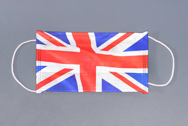 Elszigetelt orvosi maszk az Egyesült Királyság zászlajával szürke alapon. Szekrényvédő maszkok textilszűrő. Egészségügyi és orvosi koncepció. Coronavirus, vírus az Egyesült Királyságban. - Fotó, kép