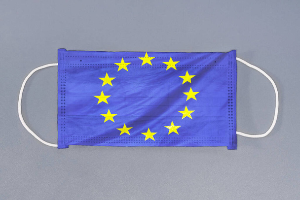 Μεμονωμένη ιατρική μάσκα με σημαία της Ευρωπαϊκής Ένωσης σε γκρι φόντο. Στενές προστατευτικές μάσκες υφασμάτινο φίλτρο. Ιατρική περίθαλψη και ιατρική έννοια. Ιός του Coronavirus στην ΕΕ. - Φωτογραφία, εικόνα