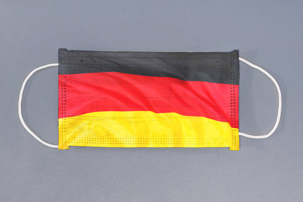 Izolovaná lékařská maska s vlajkou Německa na šedém pozadí. Closeup ochranné masky textilní filtr. Zdravotní péče a lékařská koncepce. Koronavirus, virus v Německu. - Fotografie, Obrázek