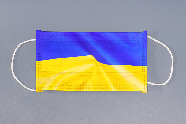 Vereinzelte medizinische Maske mit Flagge der Ukraine auf grauem Hintergrund. Nahaufnahme Schutzmasken Textilfilter. Gesundheitsfürsorge und medizinisches Konzept. Coronavirus, Virus in der Ukraine. - Foto, Bild