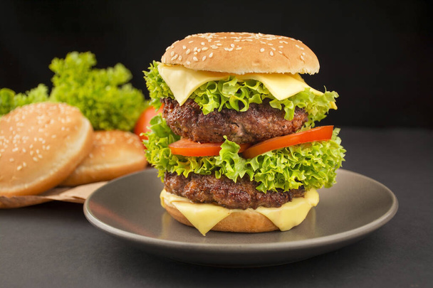 Kész hamburger marhahússal, sajttal, uborkával, friss paradicsommal és salátával. Sötét háttér. Étel háttér. Gyors kaja. Főzök. Közelkép. - Fotó, kép