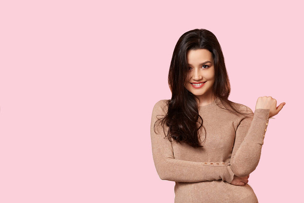 a young beautiful brunette in a light brown sweater is smiling. on a pink isolated background - Foto, afbeelding