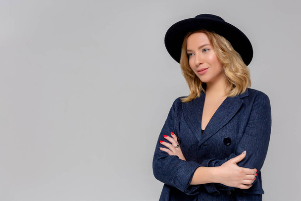 Fashionable woman in blue coat and black hat posing in studio, looking at camera. cold season. Autumn, Spring or winter look. - Photo, Image