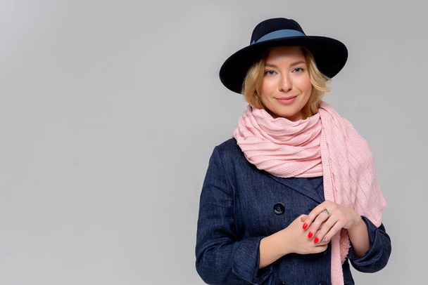 Mulher elegante em casaco azul, lenço rosa e chapéu preto posando em estúdio, olhando para a câmera. estação fria. Outono, primavera ou inverno olhar
. - Foto, Imagem