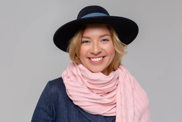Modieuze vrouw in blauwe jas, roze sjaal en zwarte hoed poseren in de studio, op zoek naar camera. Het koude seizoen. Herfst, lente of winter look. - Foto, afbeelding