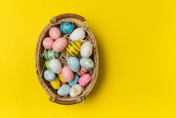 Košík s velikonočními vejci na žlutém pozadí horní pohled. Mnohobarevná sváteční vejce. - Fotografie, Obrázek