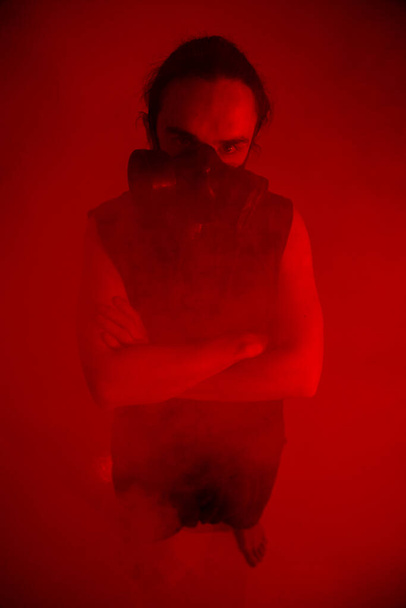 Un hombre con una máscara de gas sobre fondo rojo de pie - Foto, imagen