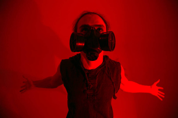 A man in a gas mask on red background looking up with hand spread and smoke - 写真・画像