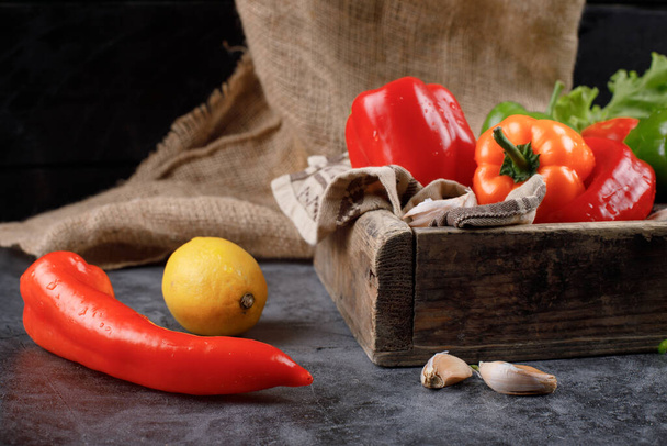 Red peppers in a wooden tray and on the table with lemon. - Photo, Image