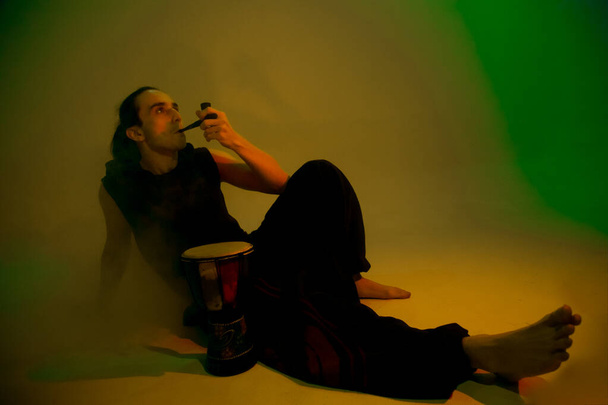 A young man smoking a pipe on green background - Fotó, kép