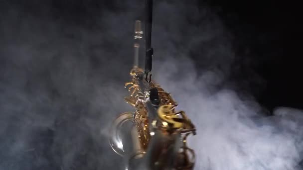 Złoty błyszczący saksofon altowy powoli porusza się na czarnym tle z dymem - Materiał filmowy, wideo