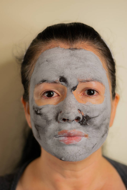 όμορφη Κολομβιανή γυναίκα καθαρίζει το δέρμα του προσώπου της με μια μαύρη μάσκα προσώπου από πηλό - Φωτογραφία, εικόνα