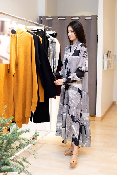 Ázsiai gyönyörű nő a grafikus ruha válassza ki az új kollekció készen áll, hogy viselje ruhák állvány a kiskereskedelmi divat áruház, amely csak nyitott márka hírek téli ősszel alkalmi stílus - Fotó, kép