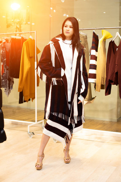 Ασιατική όμορφη γυναίκα σε μαύρο λευκό φόρεμα επιλέξτε νέα συλλογή σε έτοιμα να φορούν ρούχα rack στο κατάστημα λιανικής πώλησης μόδας που μόλις ανοίξει το εμπορικό σήμα ειδήσεων για το φθινόπωρο του χειμώνα ως casual στυλ - Φωτογραφία, εικόνα