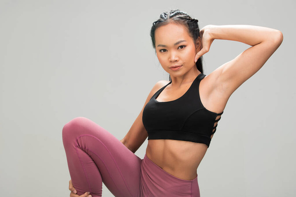 アジアタンスキンフィットネス女性運動ウォームアップストレッチアームズは黒スポーツブラ桑紫色のパンツ、スタジオ照明グレーの背景コピースペース、コンセプトウーマンはスポーツを行うことができます6パック - 写真・画像