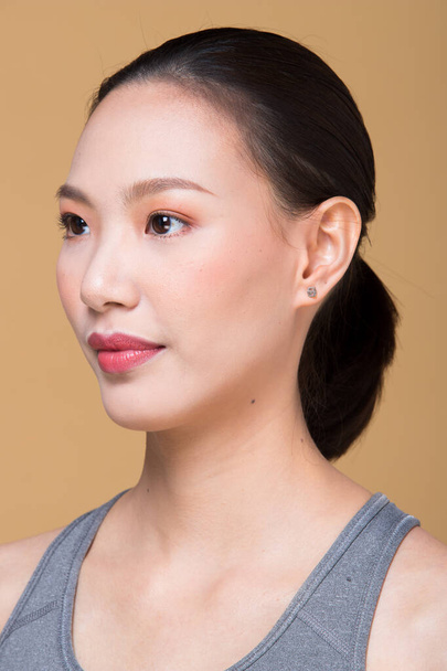 適用後のアジアの女性は、ラップヘアスタイルを構成します。レタッチなしにきび、唇、目、頬、素敵な滑らかな肌で新鮮な顔。スタジオ照明黄色ベージュマスタード背景,美学療法のための - 写真・画像