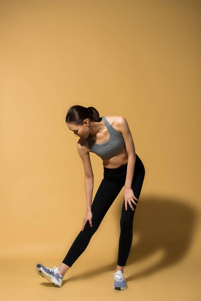 Asyalı Slim Fitness Kadını ısınma egzersizi kollarını esnetme, stüdyo sarı bej arkaplan arka plan gölge fotokopi alanı, konsept Kadın Sporcu Yapabilir 6 paket spor paketi - Fotoğraf, Görsel