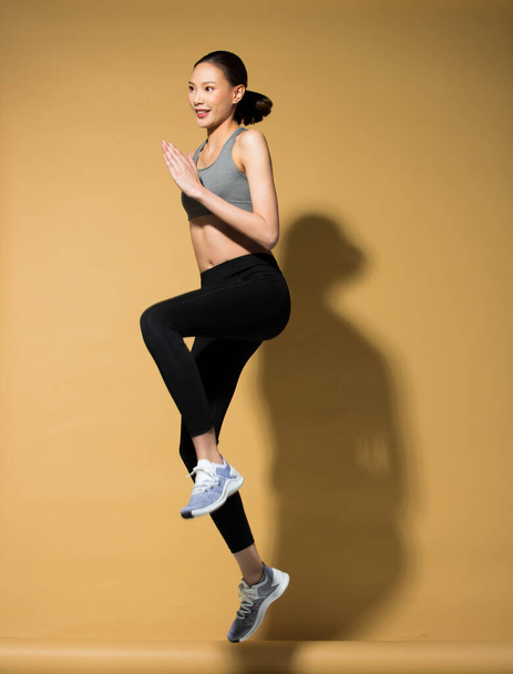 Ázsiai karcsú Fitness nő gyakorlat bemelegítés rugó ugrik lábak, stúdió világítás sárga bézs mustár háttér napernyő fénymásolás tér, koncepció Woman Can Do sportoló Sport 6 csomag - Fotó, kép