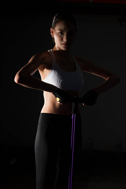 Asian slim Fitness woman extending legs resistance band in Fog Smoke Σκούρο φόντο χαμηλό περιβάλλον έκθεσης, στούντιο φωτισμού αντίγραφο χώρου, έννοια Γυναίκα μπορεί να κάνει τον αθλητισμό 6 πακέτα - Φωτογραφία, εικόνα