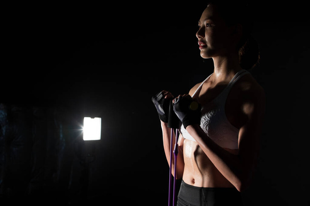 Azjatycki szczupły Fitness kobieta ćwiczenia rozciąganie nogi ramiona pas oporu we mgle dym ciemne tło niskie środowisko ekspozycji, studio oświetlenie przestrzeń kopia, koncepcja kobieta może zrobić Sport 6 paczek - Zdjęcie, obraz