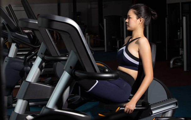 Азиатская стройная фитнес-женщина черные волосы спортивный бюстгальтер упражнения разогреть на толкающей машине велосипед велосипед в тренажерном зале. Концепция женщина может делать спортсмен спорт здоровым
 - Фото, изображение