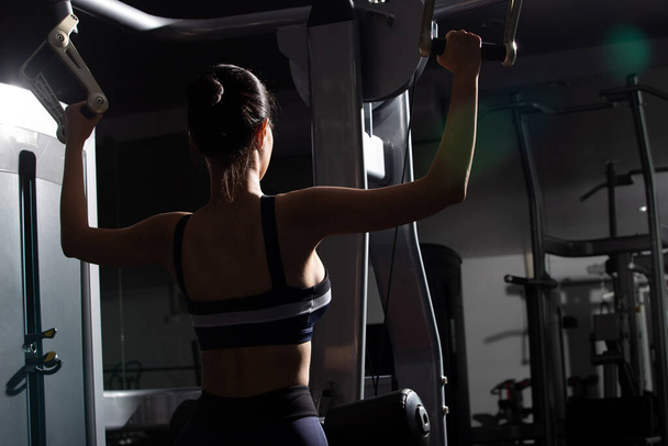 Πίσω όψη πλευρά της Ασίας λεπτή Fitness γυναίκα μαύρα μαλλιά σπορ σουτιέν άσκηση ζέσταμα για ώθηση Τραβήξτε το μηχάνημα Βάρος μυών Χέρια MultiFunction σε Fit Γυμναστήριο. Έννοια θηλυκό μπορεί να κάνει τον αθλητισμό υγιή - Φωτογραφία, εικόνα
